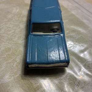 May include: A blue die-cast toy car with a metal body, featuring the word Chevrolet embossed on the front hood. The vehicle has a visible black steering wheel inside the cabin, a silver-colored front grille, and a smooth, painted exterior finish.