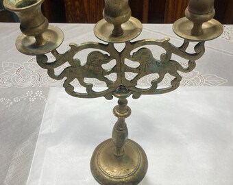 Può includere: Un candelabro in ottone con tre portacandele. Il candelabro è decorato con un disegno di due leoni che si fronteggiano. La base del candelabro è rotonda e ha un design decorativo.