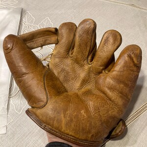 May include: A brown leather baseball glove with a worn appearance. The glove is open and the fingers are spread out.