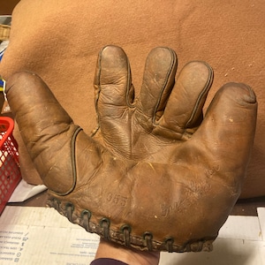 May include: A well-worn, brown leather baseball glove. The glove has visible stitching and is marked with the number "355" and the name "Ernie Walker". The glove shows signs of age and use, with creases and wear marks.