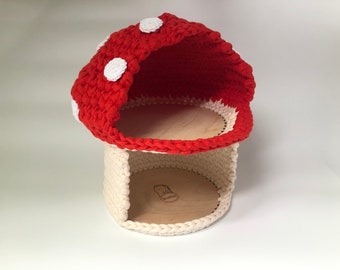 May include: A crocheted mushroom-shaped storage basket with a red top and white bottom. The basket has a white polka dot pattern on the red top and is made of yarn.