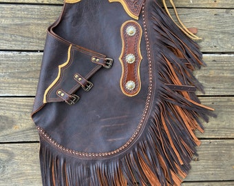 May include: Brown leather chaps with fringe, a sunflower design, and a silver buckle. The chaps have a yellow and brown trim.