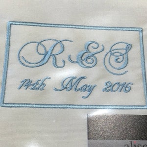 May include: Cream-coloured fabric with light blue embroidered initials "R & E" and the date "14th May 2016" within a rectangular frame. The embroidery provides a personalised touch, suitable for special occasions.