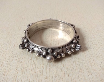 May include: A silver bangle bracelet with a decorative design of small beads and intricate patterns. The bracelet is hinged and has a clasp.