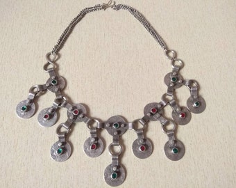 May include: A silver necklace with a chain and multiple round pendants. The pendants have green and red stones set in them.