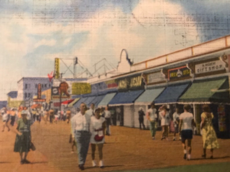 May include: A vintage postcard depicting a bustling boardwalk scene with shops and people walking along the sidewalk. The shops have colorful awnings and signs, including "Gift Shop" and "Sea Isle".