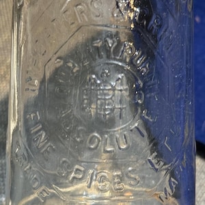 以下が含まれることがあります： 「B.M. Millar & Co. Pure Spices Fine Absolute Extract Made Chicago」と書いてあるラベルが付いた透明なガラス瓶。ラベルには、ワシのスタイリッシュな画像も描かれている。