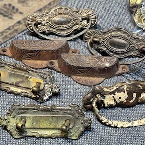 以下が含まれることがあります： 装飾的な真鍮製の引き出しノブ、鋳鉄製のノブ、リングハンドルが付いた白く塗られたノブなど、アンティークのキャビネット金具の詰め合わせです。