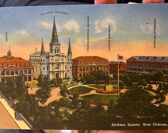 May include: A vintage postcard depicting Jackson Square in New Orleans, Louisiana. The postcard shows the St. Louis Cathedral, the Cabildo, the State Historical Museum, and the Jackson Monument. The square is surrounded by trees and buildings.