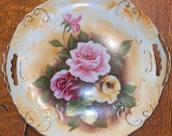 May include: A white porcelain serving platter with gold trim and a floral design featuring pink, yellow, and red roses. The platter has two handles on the sides.