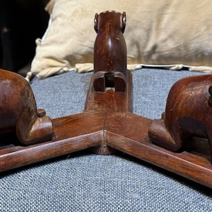 May include: A wooden bookend featuring three carved elephants. The elephants are brown and have white accents. The bookend is a decorative piece for a home or office.