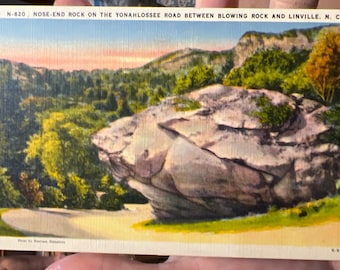 May include: A vintage postcard featuring a scenic view of a large rock formation in a wooded area. The postcard is titled "NOSE-END ROCK ON THE YONAHLOSSEE ROAD BETWEEN BLOWING ROCK AND LINVILLE. N. C."