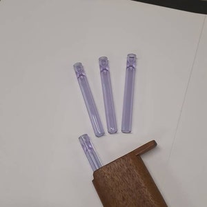 May include: Four purple glass smoking pipes with a wooden storage case. The pipes are arranged in a fan shape on a white surface.