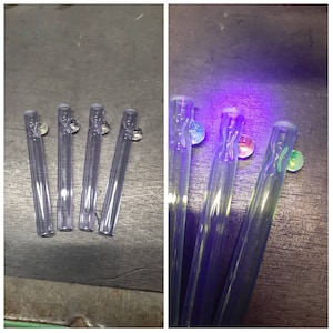 May include: Four clear glass tubes with a small, round, colorful glass bead at the end of each tube. The tubes are shown in normal light and under a black light, which reveals the beads glowing in different colors.