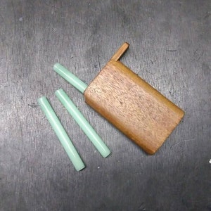 May include: A wooden box with a hinged lid, open to reveal three light green cylindrical objects. The box is made of a dark brown wood with a natural grain pattern.