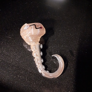 May include: A translucent, light brown, glass octopus figurine with a red eye and a black line on the head. The octopus has eight tentacles with white dots on each tentacle.