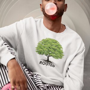 May include: A white sweatshirt with a green tree graphic and the word "ROOTED" printed below it. The person wearing the sweatshirt is blowing a bubble with pink bubble gum.