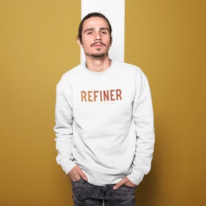 May include: A gray sweatshirt with the word "REFINER" printed in orange and brown letters on the front. The text is in a bold, sans-serif font.
