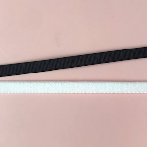 Puede incluir: Dos tiras de cinta elástica, una negra y otra blanca, se muestran sobre un fondo rosa claro. La cinta negra es de tejido texturizado. La cinta blanca tiene una textura suave y difusa.