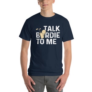 Op de afbeelding: Een marineblauw t-shirt met een witte afbeelding waarop "Talk Birdie To Me" staat en een cartoonafbeelding van een golfbal in een cocktailglas.
