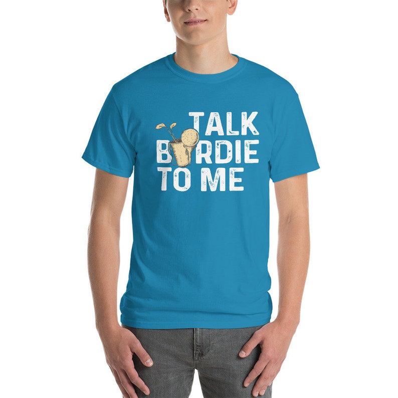 Op de afbeelding: Een turquoise blauw t-shirt met een witte afbeelding waarop staat "Talk Birdie To Me". De afbeelding toont een cartoon van een golfbal in een golfbeker.