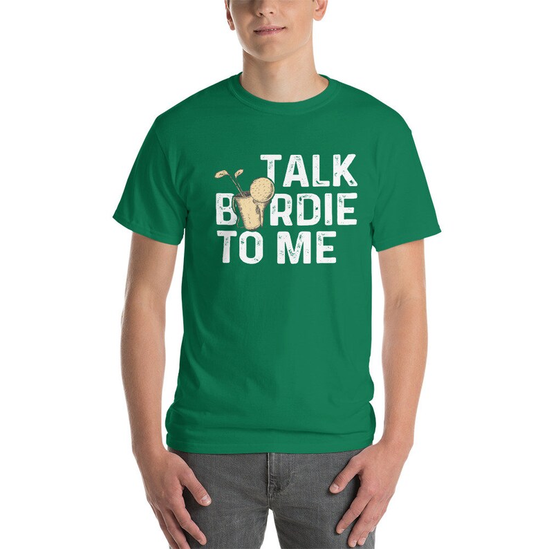 Op de afbeelding: Groen T-shirt met witte tekst die "Talk Birdie To Me" luidt. De tekst is in een verweerd lettertype. Een kleine afbeelding van een golfbal in een hole bevindt zich boven het woord "Birdie".