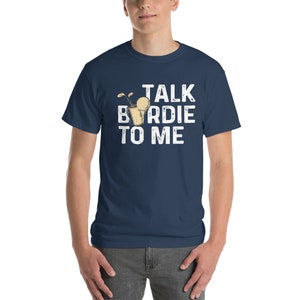 Op de afbeelding: Een marineblauw t-shirt met een witte afbeelding waarop "Talk Birdie To Me" staat. De afbeelding bevat een cartoon van een golfbal in een glas met een rietje.