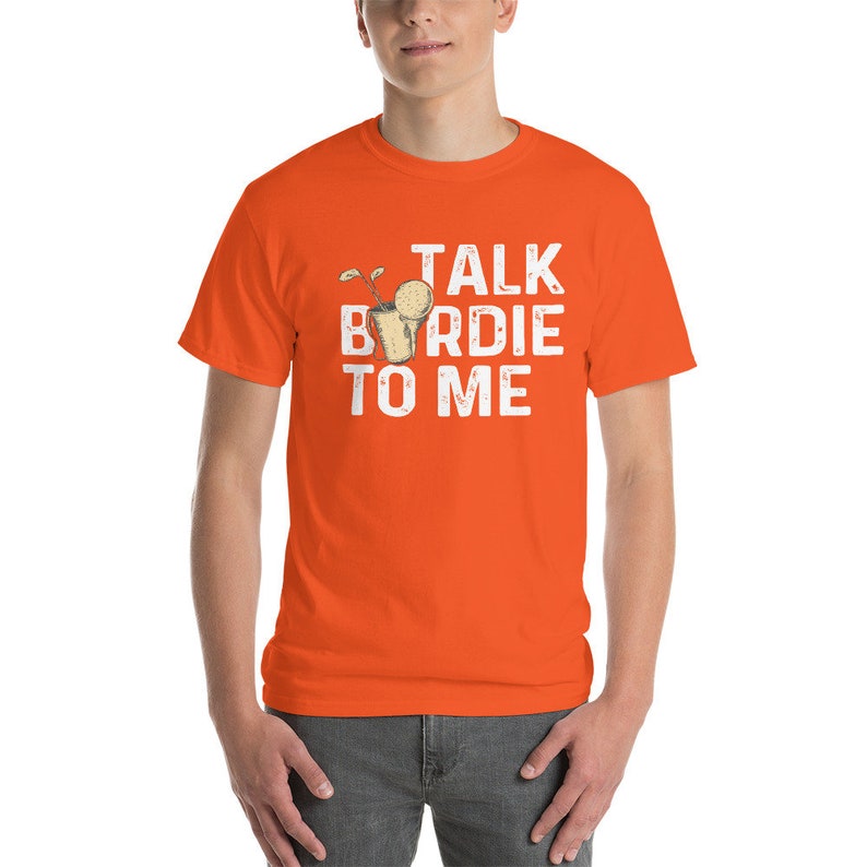 Op de afbeelding: Oranje T-shirt met een witte afbeelding van een golfclub en de tekst "TALK BIRDIE TO ME".