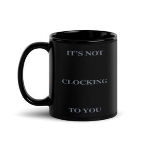 May include: Black ceramic mug with the text "IT'S NOT CLOCKING TO YOU" in light gray. The mug has a curved handle and a glossy finish. The mug is designed for hot or cold beverages.