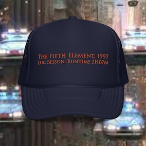 May include: A navy blue trucker hat with a mesh back. The hat has orange embroidered text that reads "THE FIFTH ELEMENT. 1997 LUC BESSON. RUNTIME 2H07M".