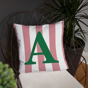 May include: A pink and white striped throw pillow with a large green letter A in the center.