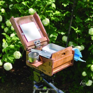 May include: A wooden artist's box with a hinged lid, mirror, and metal tray. The box is open, revealing compartments for supplies. The box is mounted on a tripod, with a blue cloth hanging on the side. The text "Only Box Included" is at the bottom.