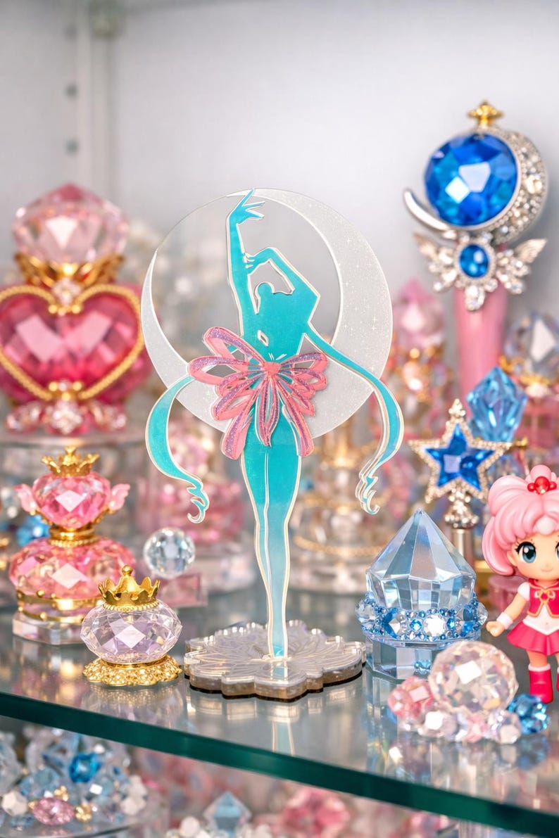 K&ouml;nnte beinhalten: T&uuml;rkisfarbene Silhouette einer Ballerina mit rosa Schleife, vor einem Halbmond. Umgeben von rosa und blauen Kristallfiguren, darunter ein Sternenstab und Parf&uuml;mflaschen, die eine skurrile Darstellung schaffen.