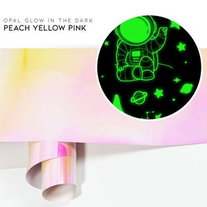 May include: A roll of glow-in-the-dark wallpaper with an astronaut and stars design. The wallpaper is peach, yellow, and pink.