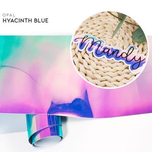 May include: A sheet of iridescent opal vinyl in a hyacinth blue color. The vinyl is folded in half and the top half is rolled up. The vinyl is a holographic material with a rainbow effect. The vinyl is a popular material for crafting and DIY projects.