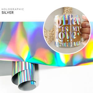 May include: A roll of holographic silver vinyl with a rainbow iridescent sheen. The vinyl is rolled up and the end is visible. A clear glass mug with the text "Coffee is my love" in a holographic silver vinyl is shown in the background.