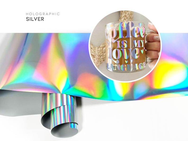 May include: A roll of holographic silver vinyl with a rainbow iridescent sheen. The vinyl is rolled up and the end is visible. A clear glass mug with the text "Coffee is my love" in a holographic silver vinyl is shown in the background.