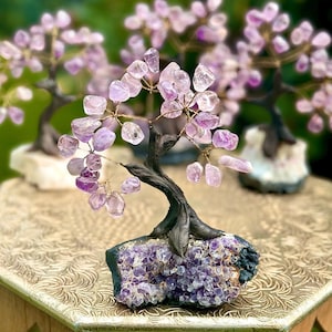 May include: Amethyst crystal tree with a purple druzy base. The tree is made of wire and amethyst crystals. The tree is on a gold table with a floral pattern.