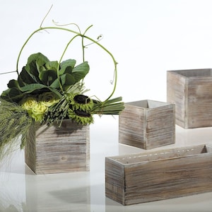 May include: Four wooden boxes in various sizes, painted white with a distressed finish. The boxes are empty and arranged on a white surface. The largest box is filled with a floral arrangement of green cabbage, yellow roses, and sunflowers.