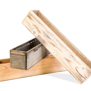 May include: Three wooden planter boxes, one is light brown, one is dark brown, and one is a light natural wood color. The boxes are stacked on top of each other.