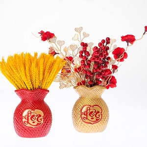 May include: Two red and gold decorative vases shaped like money bags with the word "Lộc" written on them. The red vase holds a bunch of yellow wheat stalks and the gold vase holds a bouquet of red berries and red flowers.