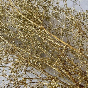 May include: Close-up of a bundle of golden, glitter-covered decorative branches. The branches are thin and delicate, with small, round, glittery accents. The overall effect is a shimmering, festive display, perfect for holiday or event decor.