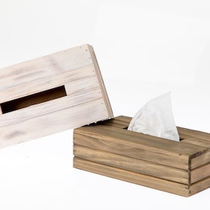May include: A wooden tissue box holder with a whitewashed lid and a natural wood base. The lid is open and a white tissue is visible inside.