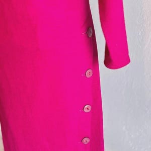 May include: A vibrant fuchsia long-sleeved garment featuring a vertical row of four matching circular buttons aligned along the side seam. The fabric has a smooth, solid texture, and the design includes a simple, clean silhouette with long sleeves.