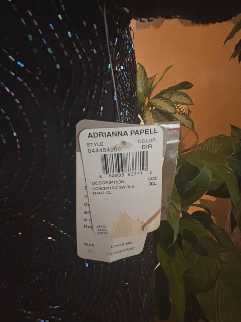 May include: Black dress with concentric swirls design, adorned with iridescent sequins. The tag reads "Adrianna Papell" and indicates size XL. The dress has a BIR color code.