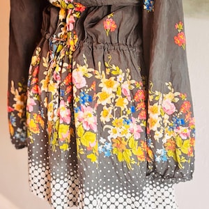 Puede incluir: Vestido gris oscuro con mangas largas y cintura ce&ntilde;ida. El vestido est&aacute; adornado con un vibrante estampado floral en tonos rosa, amarillo, azul y naranja. La falda presenta un dise&ntilde;o de lunares blancos.