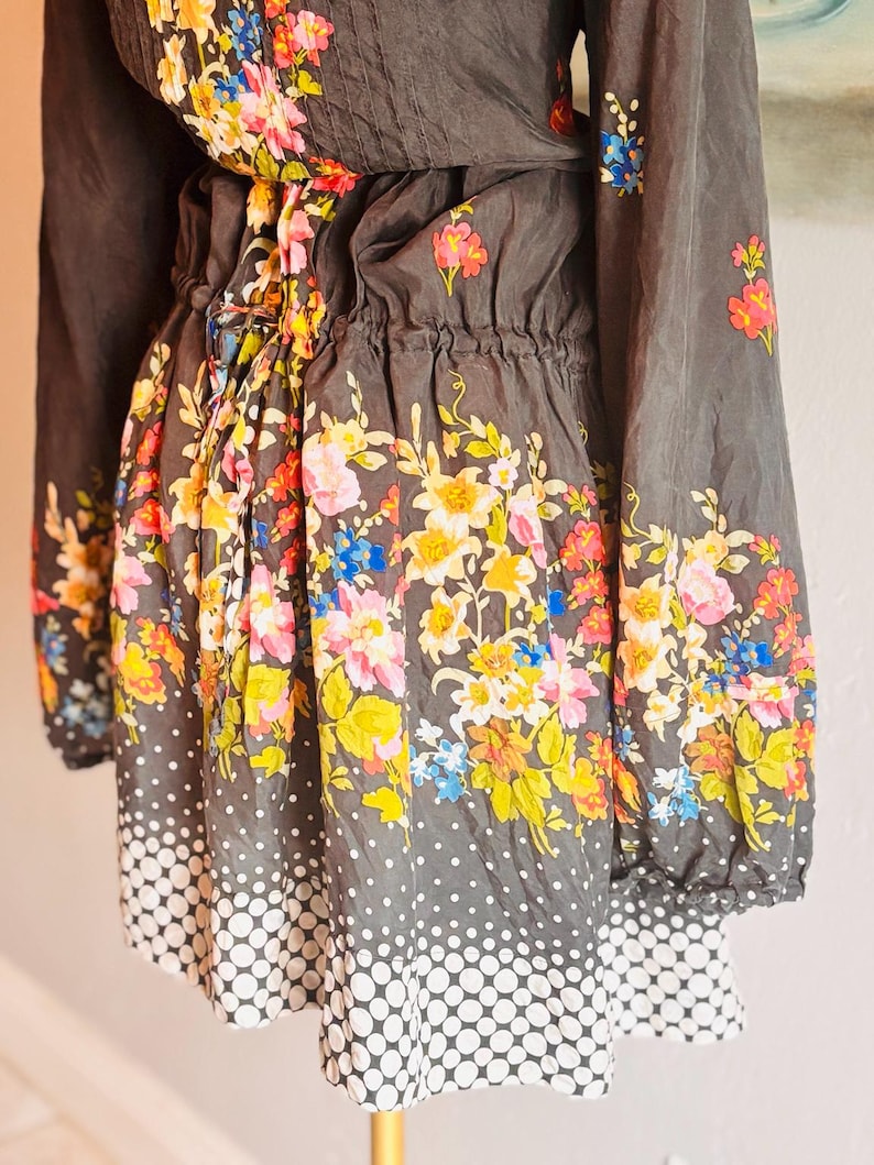 Puede incluir: Vestido gris oscuro con mangas largas y cintura ce&ntilde;ida. El vestido est&aacute; adornado con un vibrante estampado floral en tonos rosa, amarillo, azul y naranja. La falda presenta un dise&ntilde;o de lunares blancos.