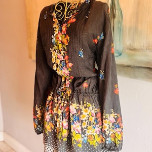 Puede incluir: Un vestido gris oscuro con estampado floral. El vestido tiene mangas largas, cintura con cord&oacute;n y dobladillo de lunares blancos. El dise&ntilde;o floral presenta una variedad de flores coloridas.