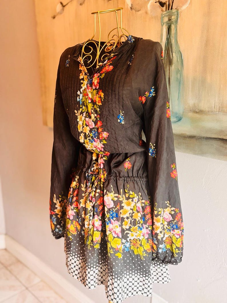Puede incluir: Un vestido gris oscuro con estampado floral. El vestido tiene mangas largas, cintura con cord&oacute;n y dobladillo de lunares blancos. El dise&ntilde;o floral presenta una variedad de flores coloridas.