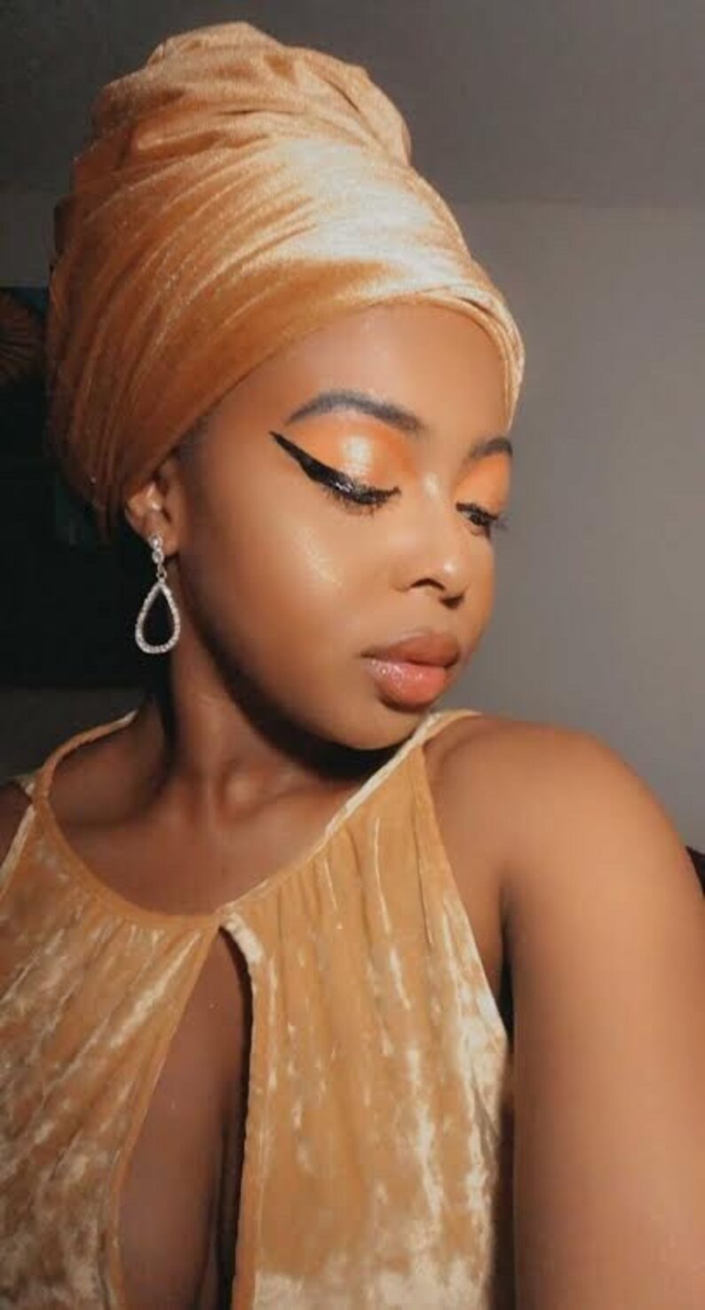 woman wearing a gold velvet head wrap with her eyes closed